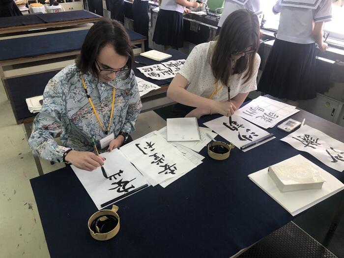 6月13日(木)グローバルインターンシップの留学生2人が漢字名をもらって書道の練習をしています。